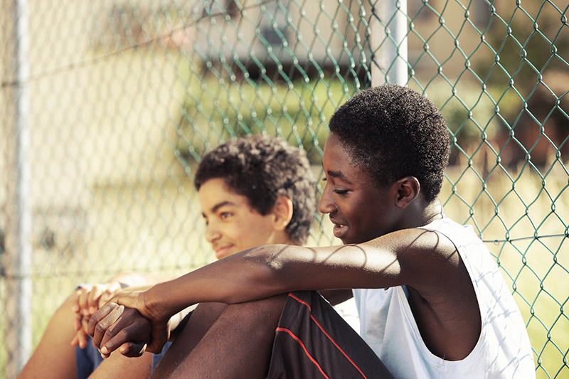 teen boys resting against a chainlink fence
